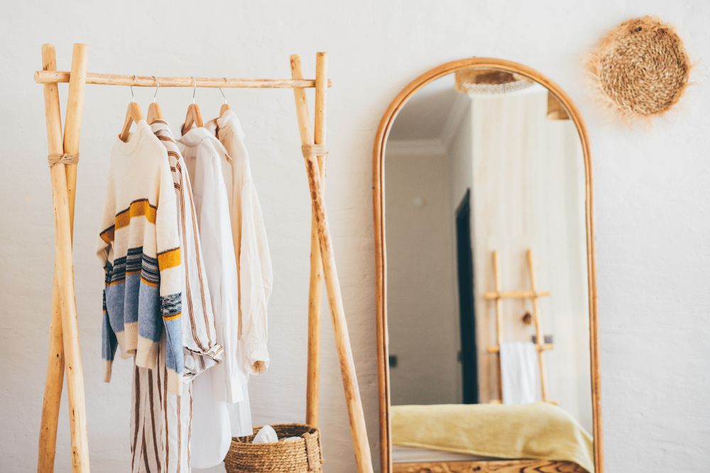 Clothes hanging on a hangers near a mirror at home.