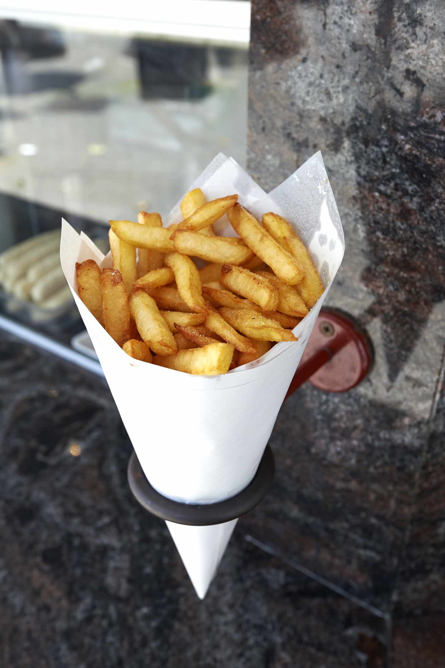 belgian fries in a paper cup hanging from the wall at a friterie