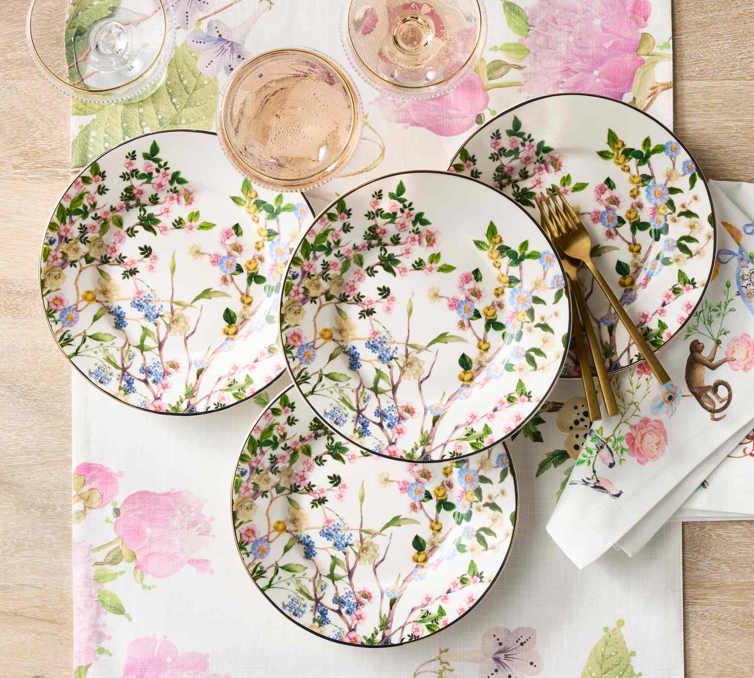 Four floral-themed dinner plates arranged on a table with matching tablecloth and napkins, complemented by glassware and utensils