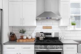 Modern kitchen with white cabinets a stainless steel stove and a counter with wooden utensils and a potted plant