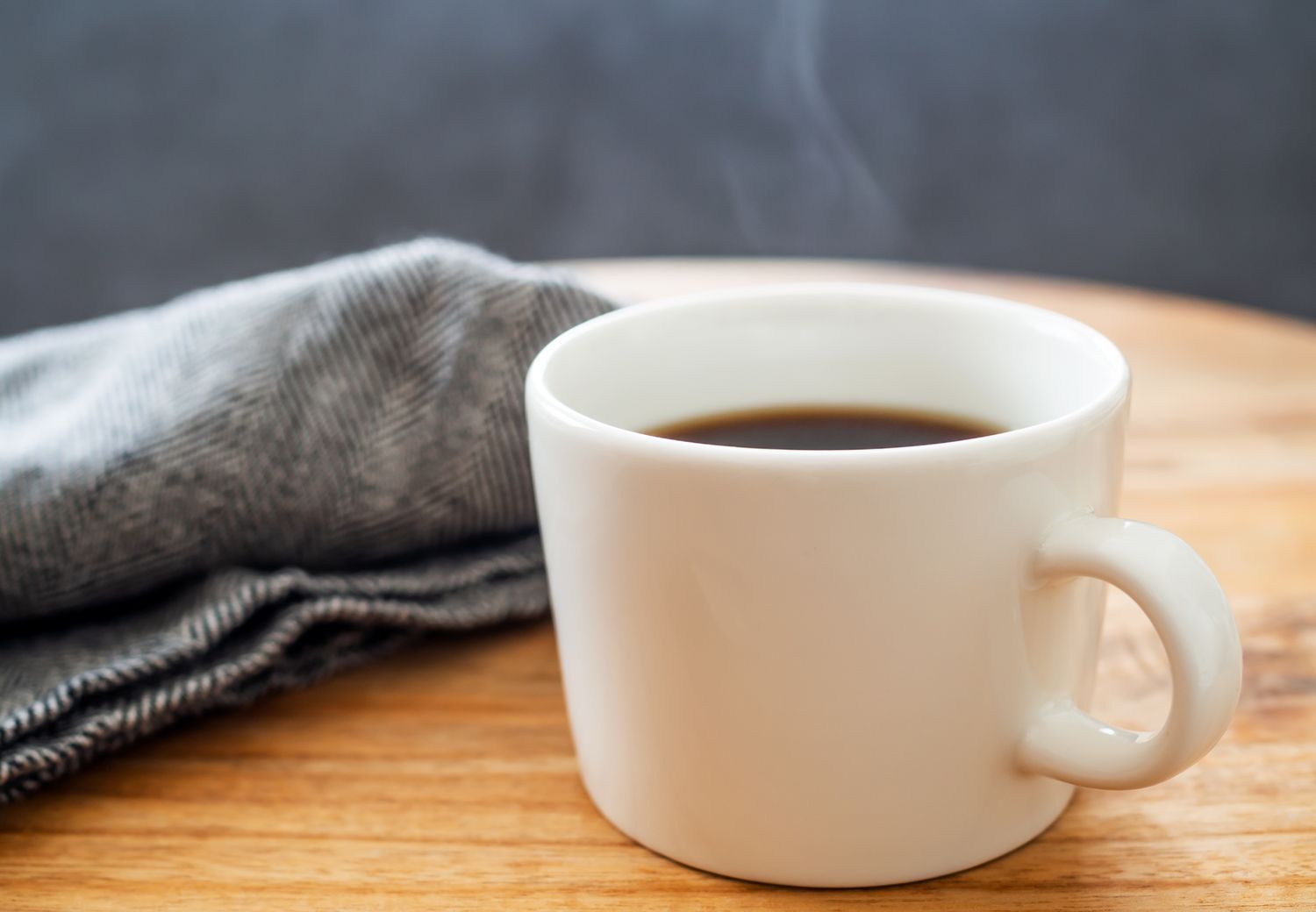 A cup of coffee on a wooden table next to a folded cloth napkin