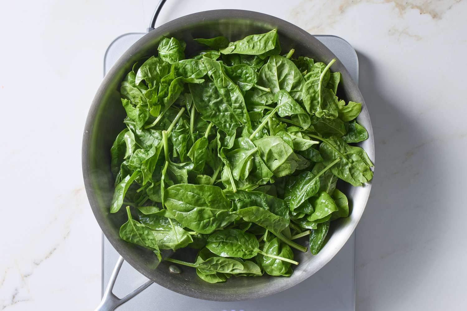 Fresh spinach leaves in a pan being prepared to steam on a stovetop