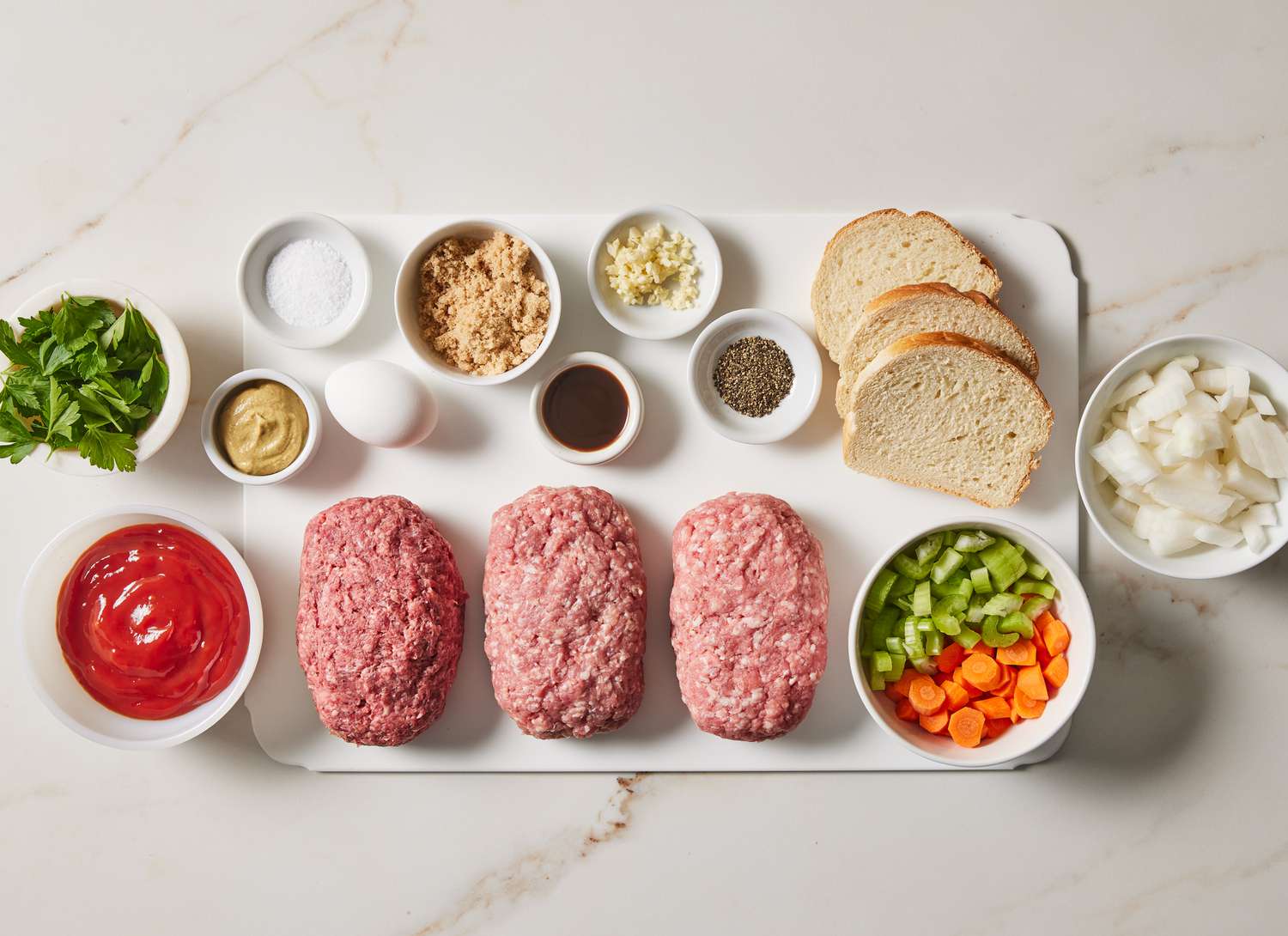 raw meatloaf ingredients on a white cutting board with bowls 