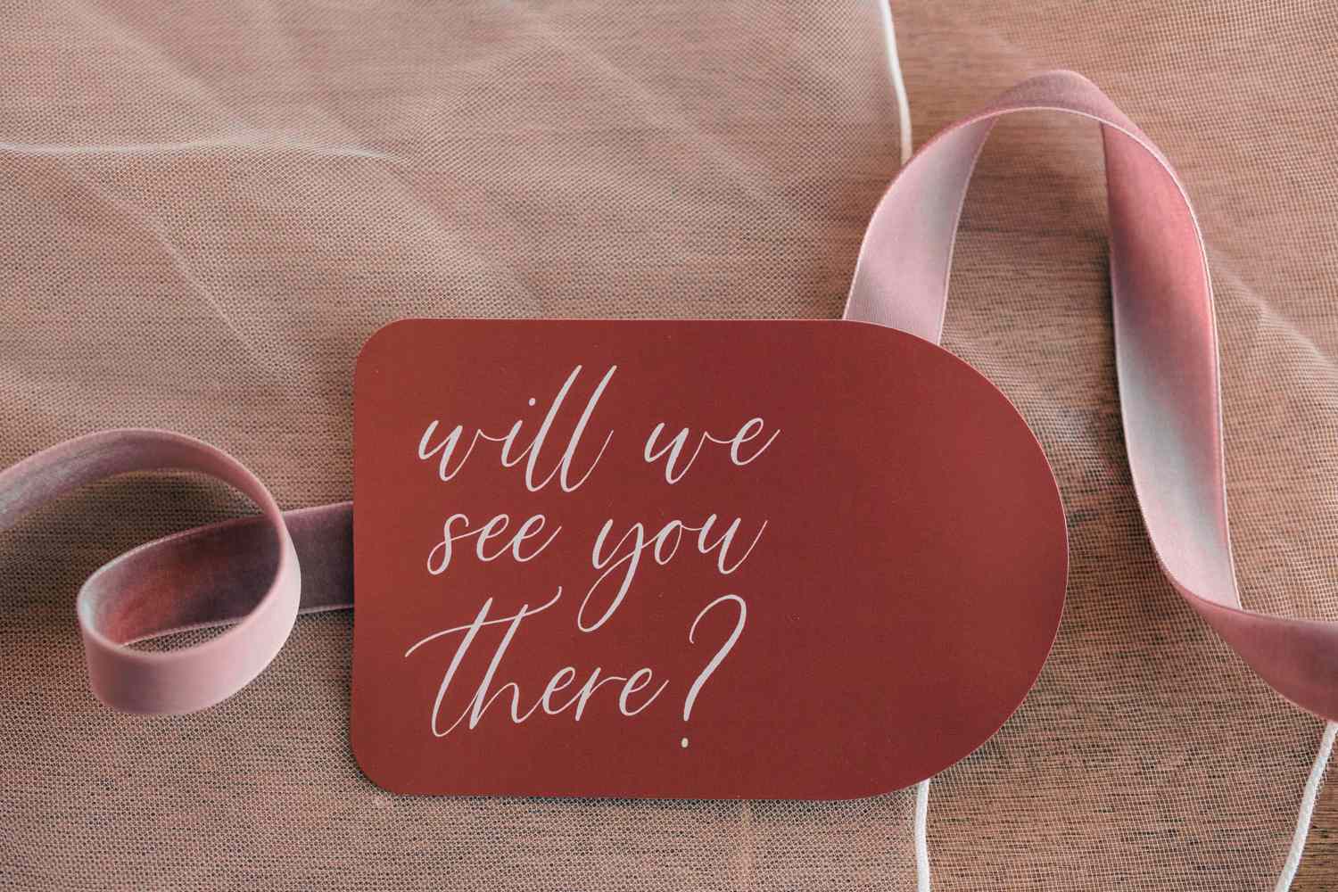 A card with the text will we see you there placed on fabric and next to a ribbon