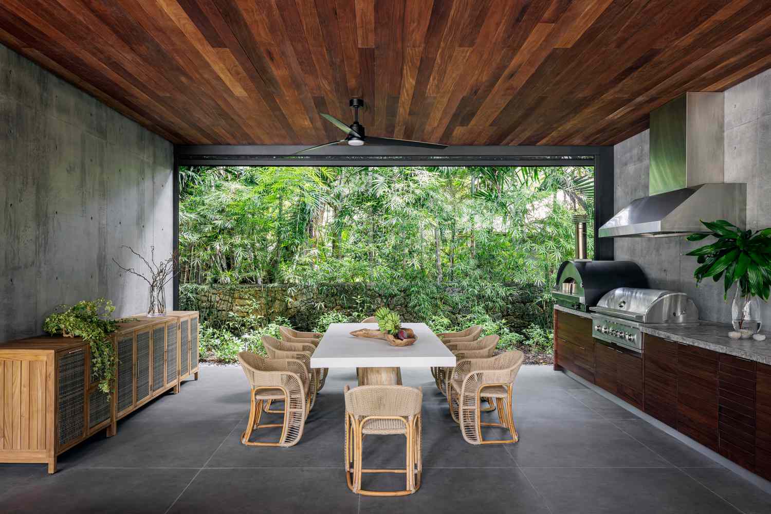 a concrete and wood patio with central dining table looks out on a green yard