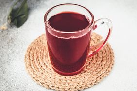 A glass mug with cherry juice resting on a woven coaster