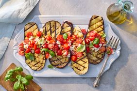 Grilled eggplant slices topped with diced tomatoes, feta cheese, and basil, served on a white platter