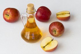 apple cider vinegar in glass bottle with whole and halved red apples