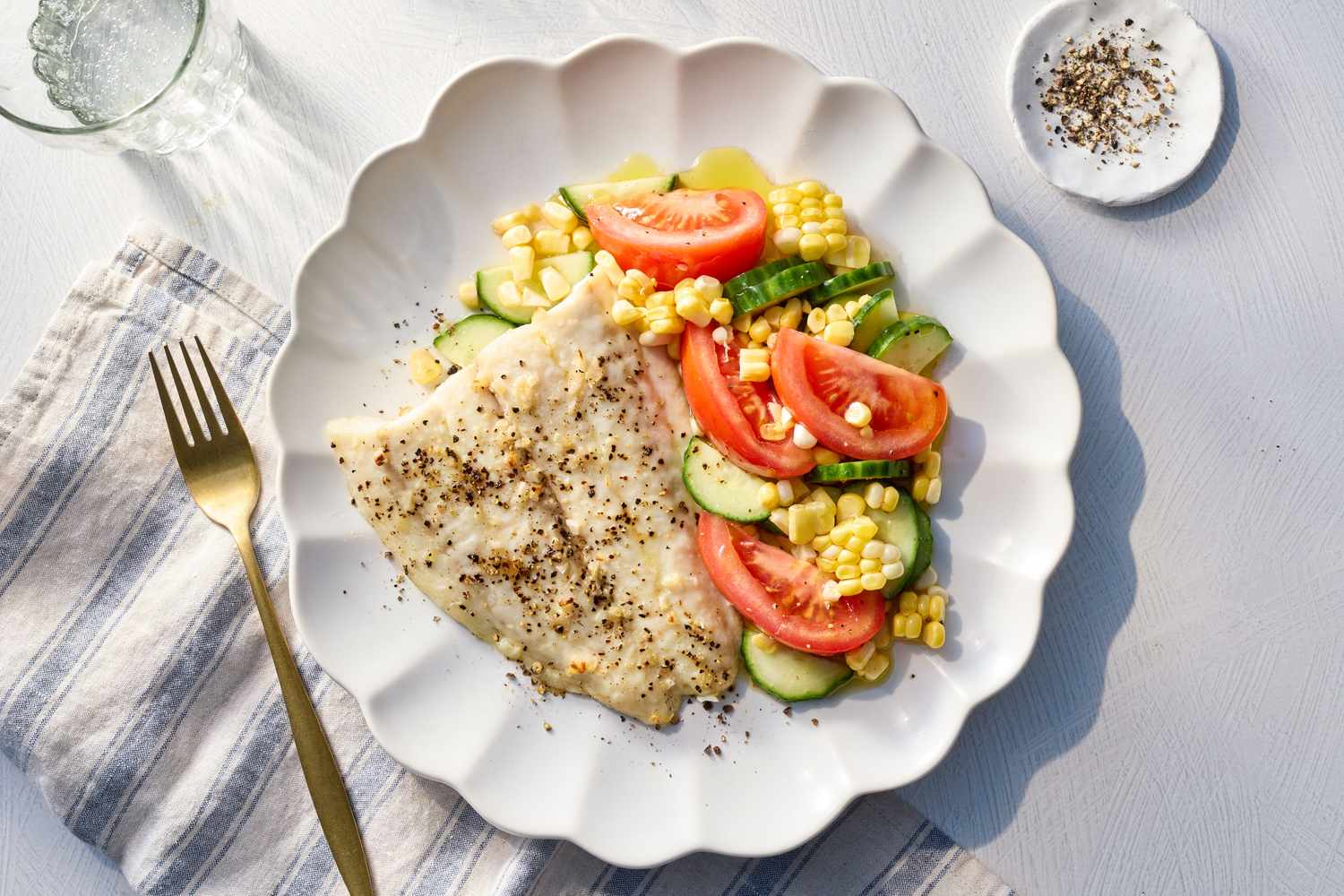A plate with broiled fish and a summer salad with tomatoes, cucumbers, and corn