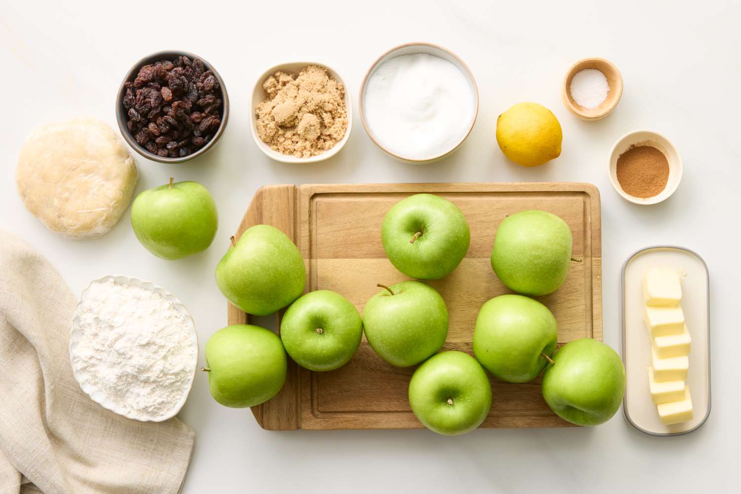 Ingredients for making apple crumble pie including green apples flour raisins sugar butter and spices arranged on a table