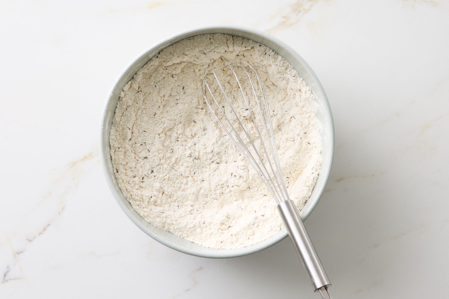 Bowl with dry ingredients and a whisk on a marble surface