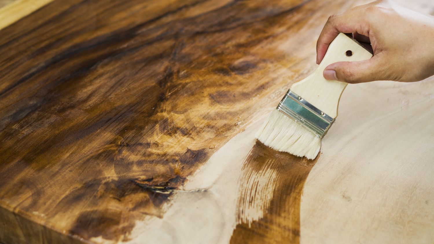 A hand applying wood finish with a brush on a wooden surface