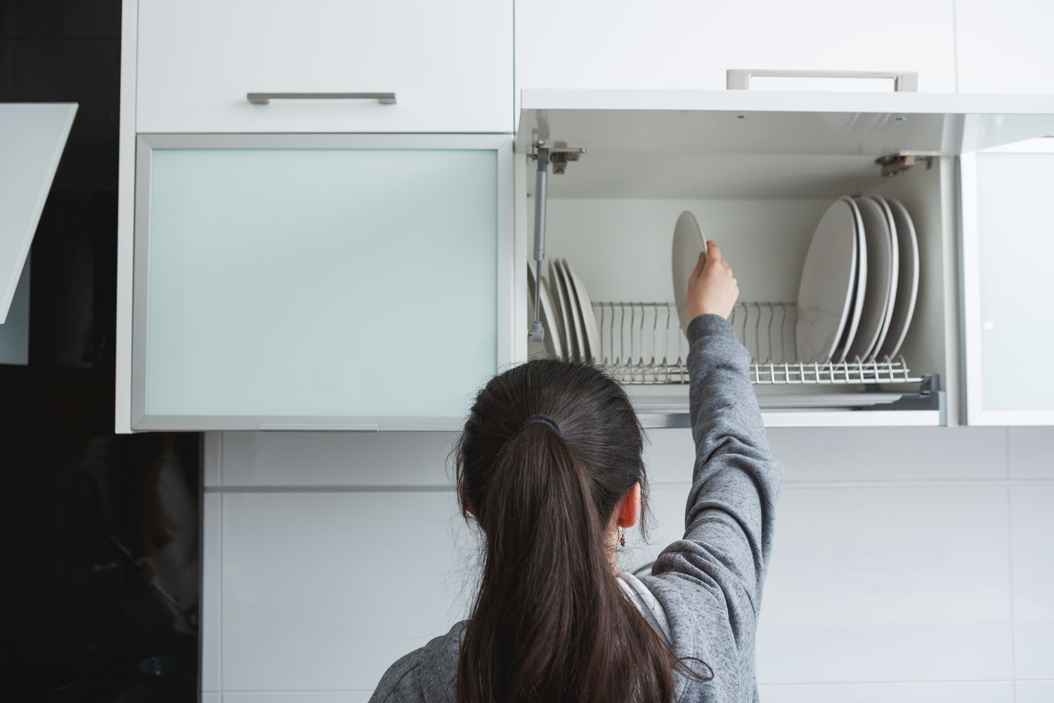 Person reaching into a kitchen cupboard with plates on a rack