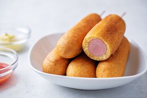 A white bowl containing several corn dogs one cut to show the inside