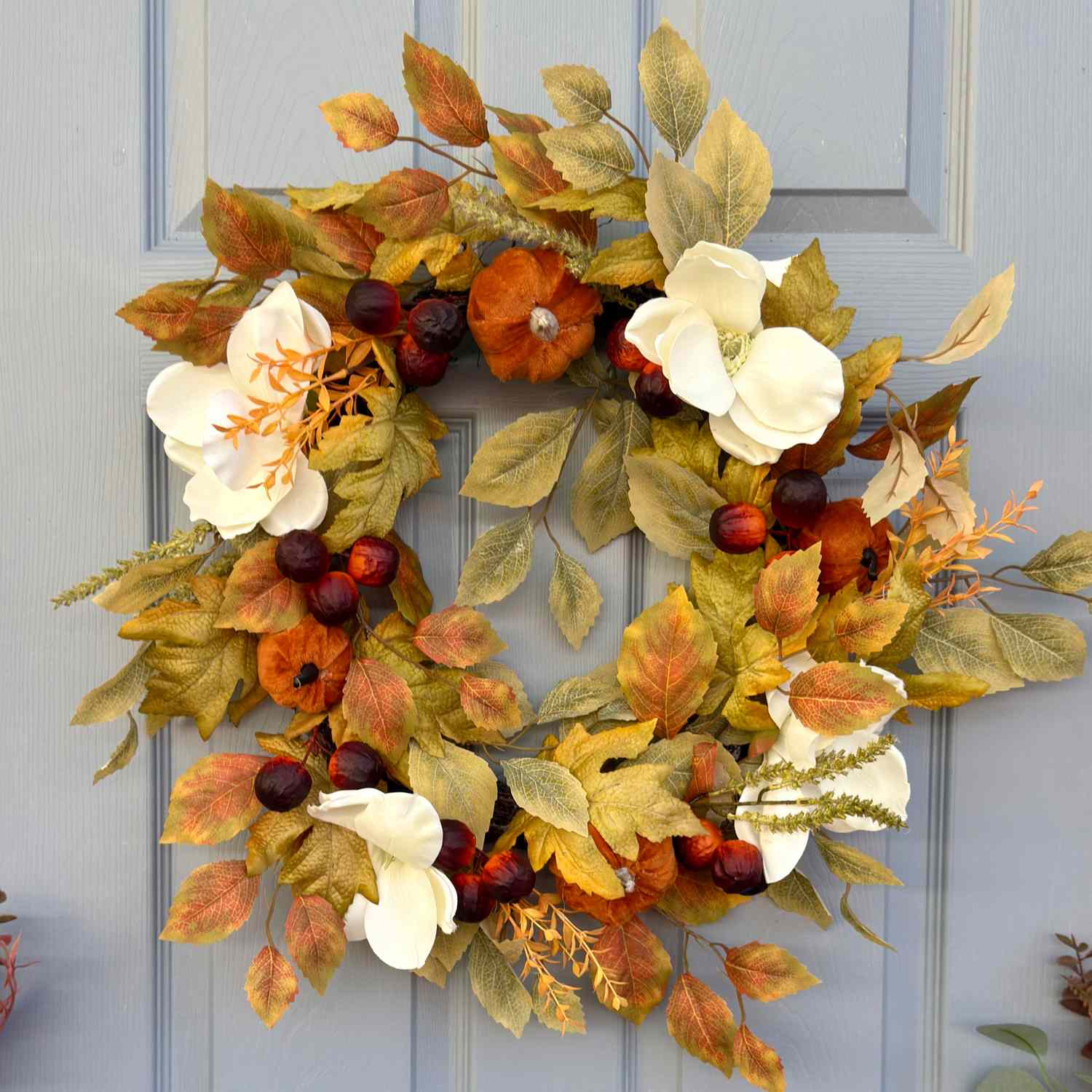A decorative wreath with autumn leaves flowers and fruits mounted on a door