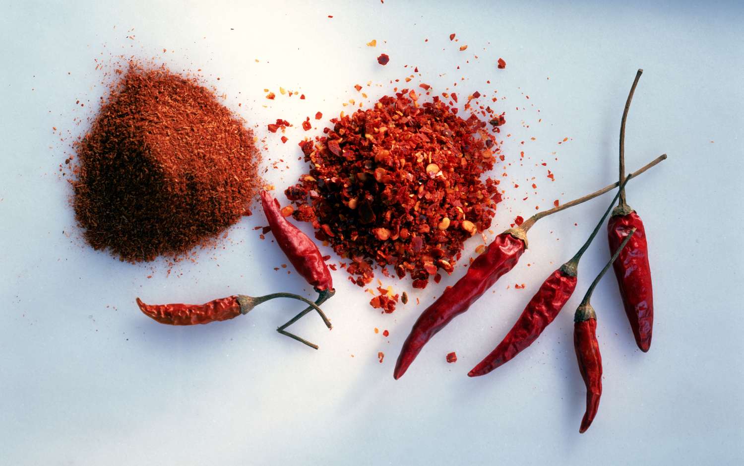 chile powder, chile-flakes, and dried chiles on blue surface