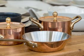 Copper pots and pans on a wooden surface arranged with other kitchenware