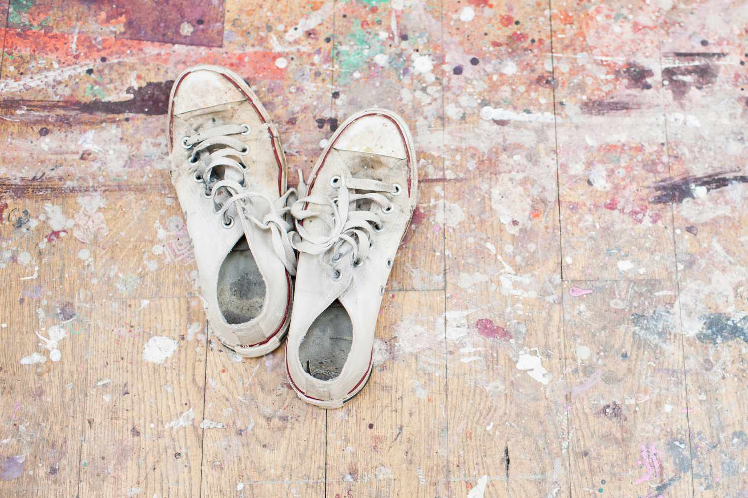 A pair of worn sneakers on a wooden floor with paint splatters