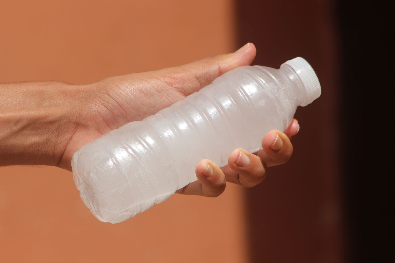 A hand holding a small transparent ridged plastic bottle with a white cap