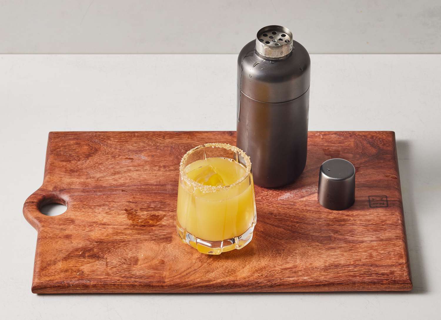 a cocktail and a metal cocktail shaker on wooden cutting board