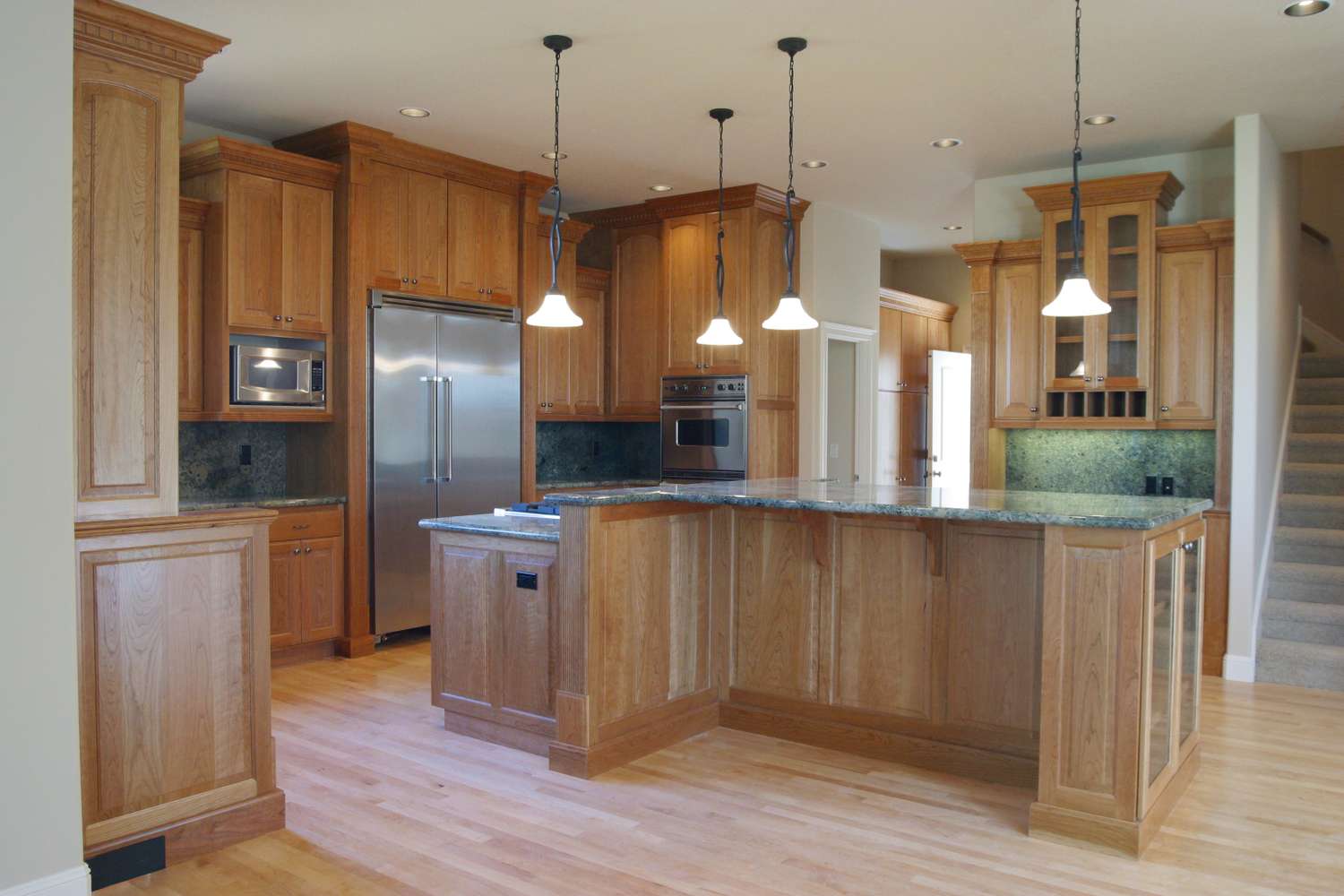 A spacious kitchen with wooden cabinets and an island pendant lights hanging above the countertop and stainless steel appliances