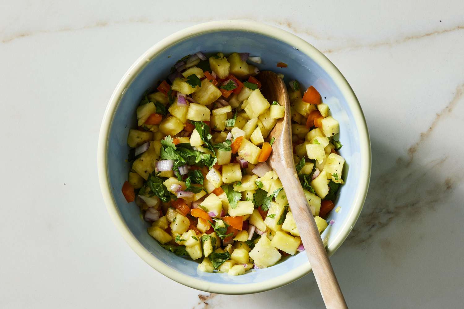 Pineapple salsa in bowl with wooden spoon