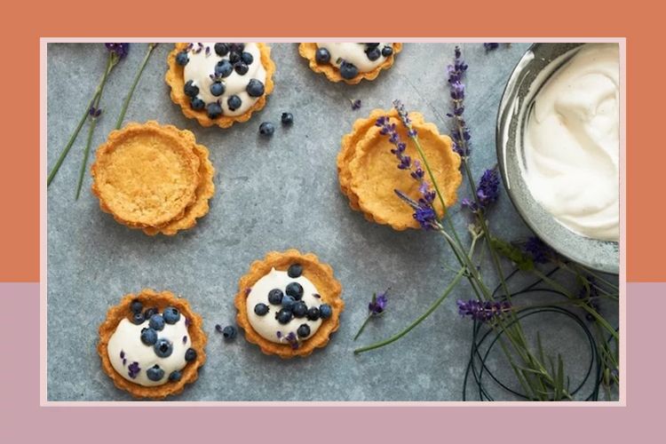 Tarts with whipped cream and blueberries lavender sprigs and a bowl of cream