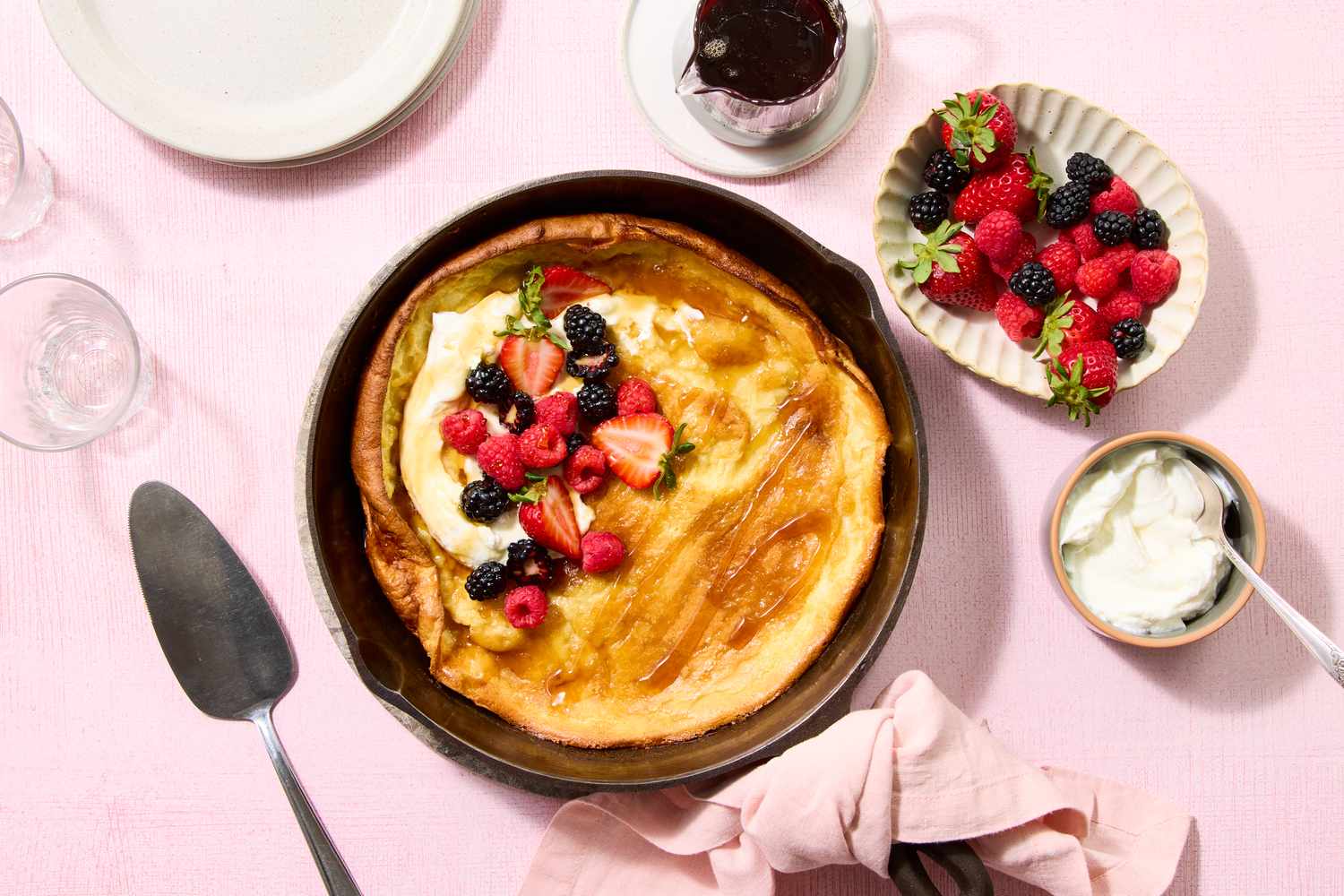 Dutch baby pancake topped with mixed berries and cream set in a pan with accompaniments