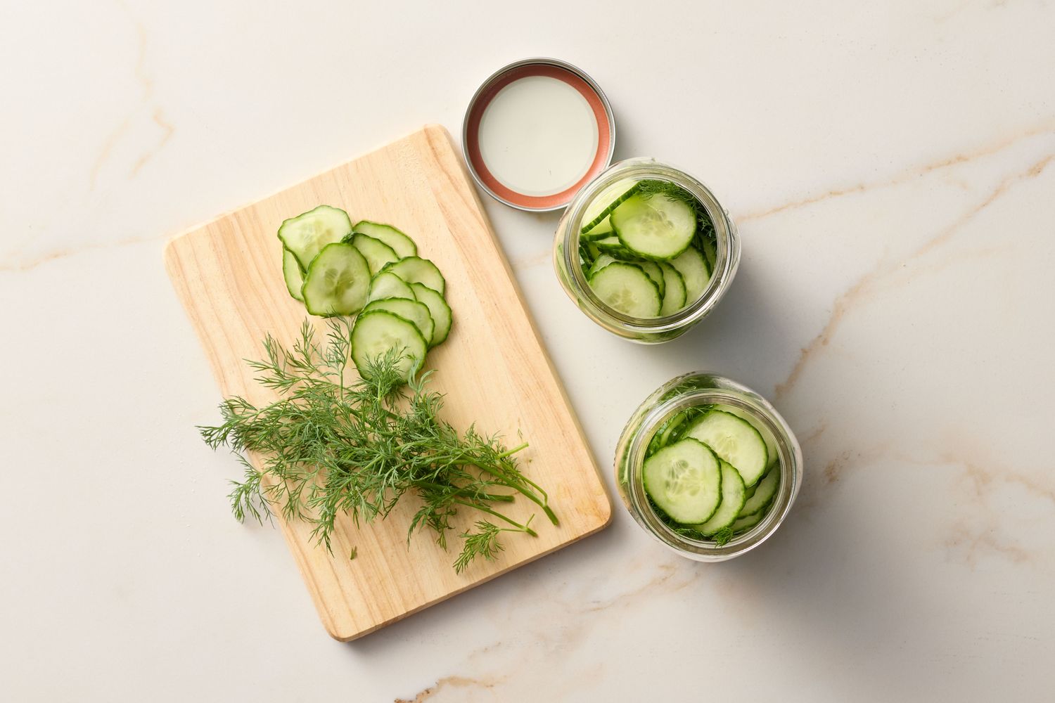 Sliced cucumbers on a cutting board accompanied by jars of prepared pickles