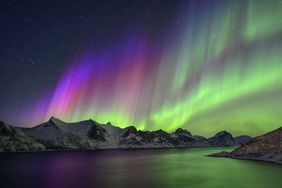 Northern lights over a mountain range and water under a starlit sky