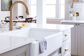 Farmhousestyle kitchen sink with a towel draped over the front surrounded by a bright kitchen with white countertops