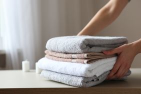 A person arranging a stack of folded towels on a table with light background