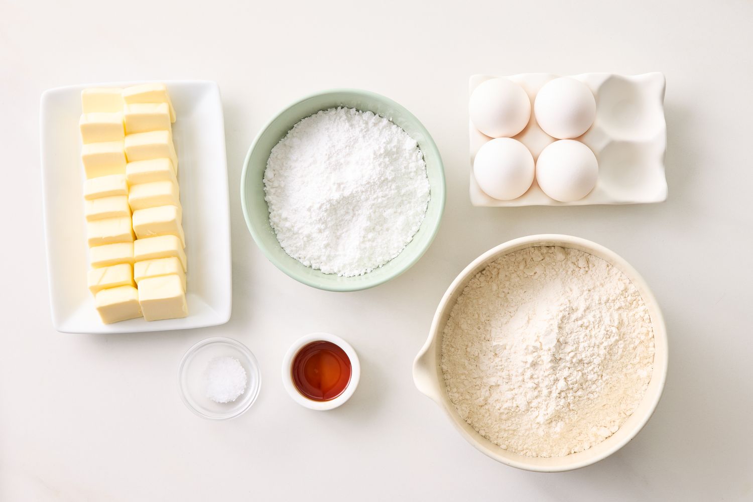 Ingredients including butter powdered sugar eggs vanilla and flour arranged on a counter