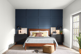 A bedroom with a wooden bed frame, blue paneled accent wall, bedside tables, and a window with natural light