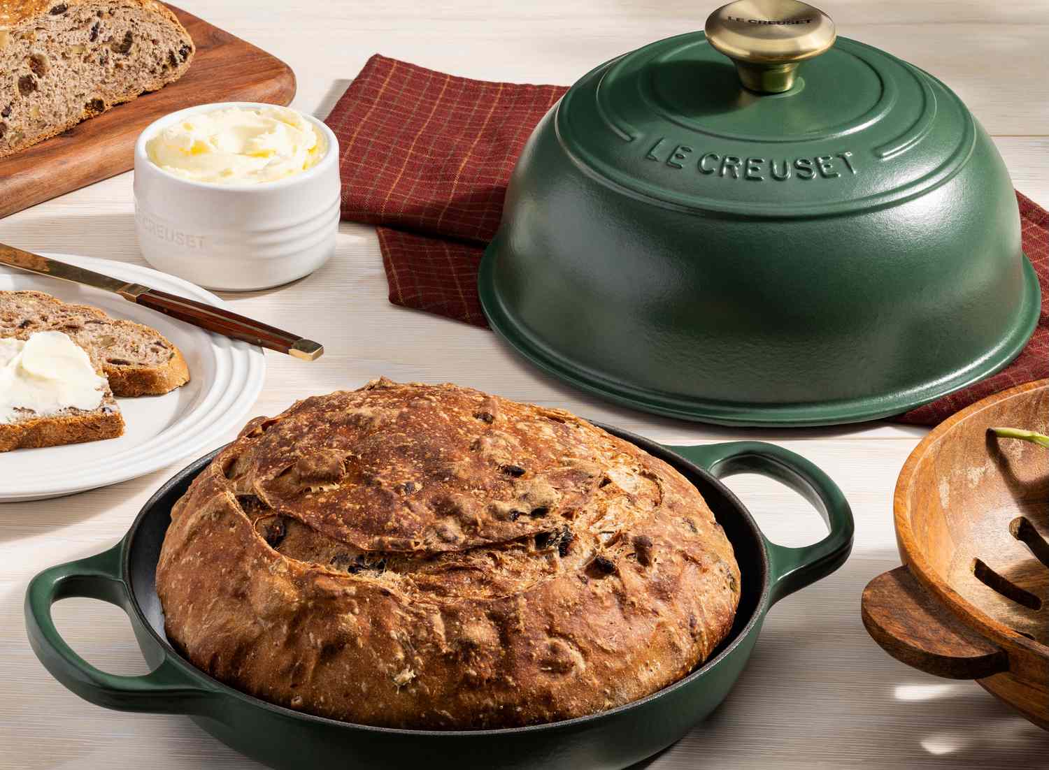 A loaf of bread in a green cast iron pot beside butter and bread slices