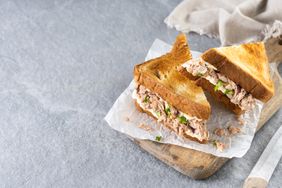 Two halves of a tuna salad sandwich placed on a wooden board with parchment paper