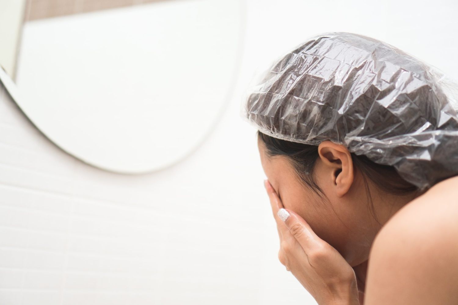 Young woman wearing a shower cap and washing face in the bathroom