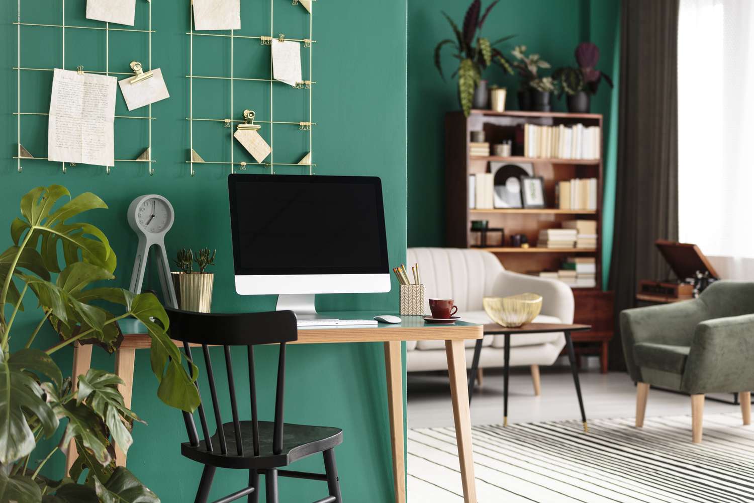 A home office setup with a desk chair computer and bookshelves adorned with plants and wall decorations in a brightly lit room