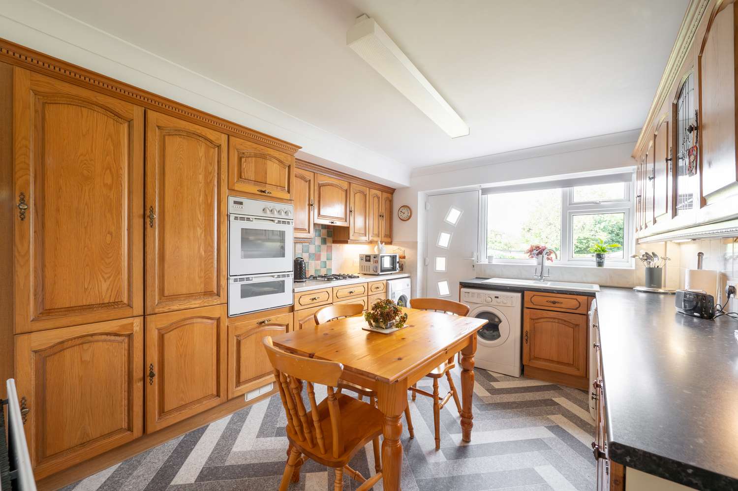 A kitchen with wooden cabinets a dining table with chairs appliances and a window letting in natural light