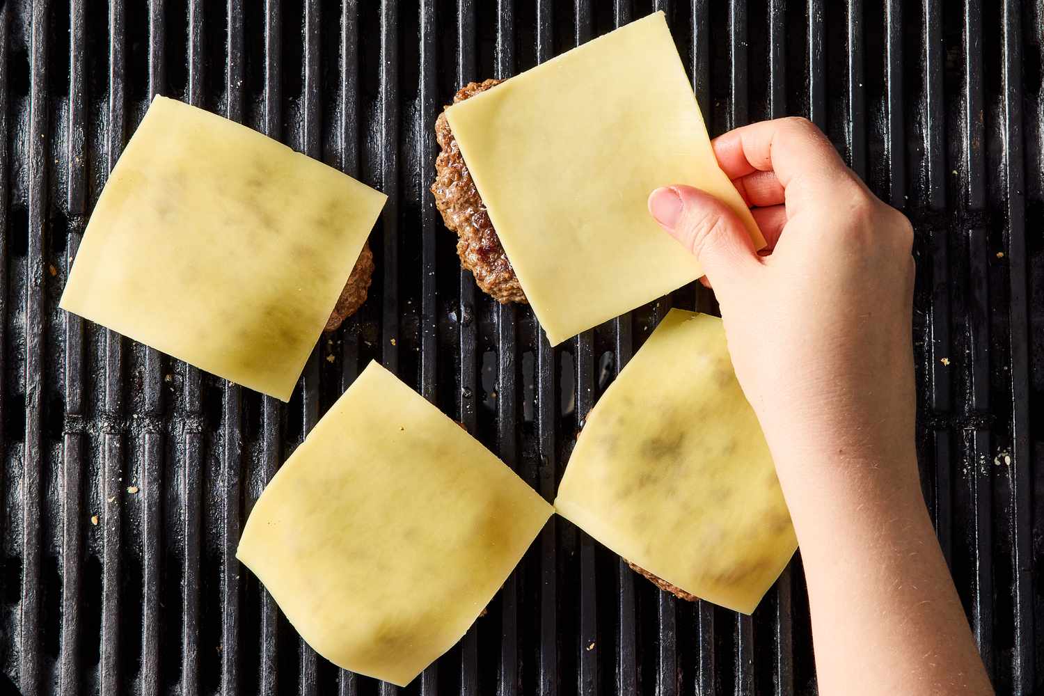 Person placing cheese slices on burgers on a grill