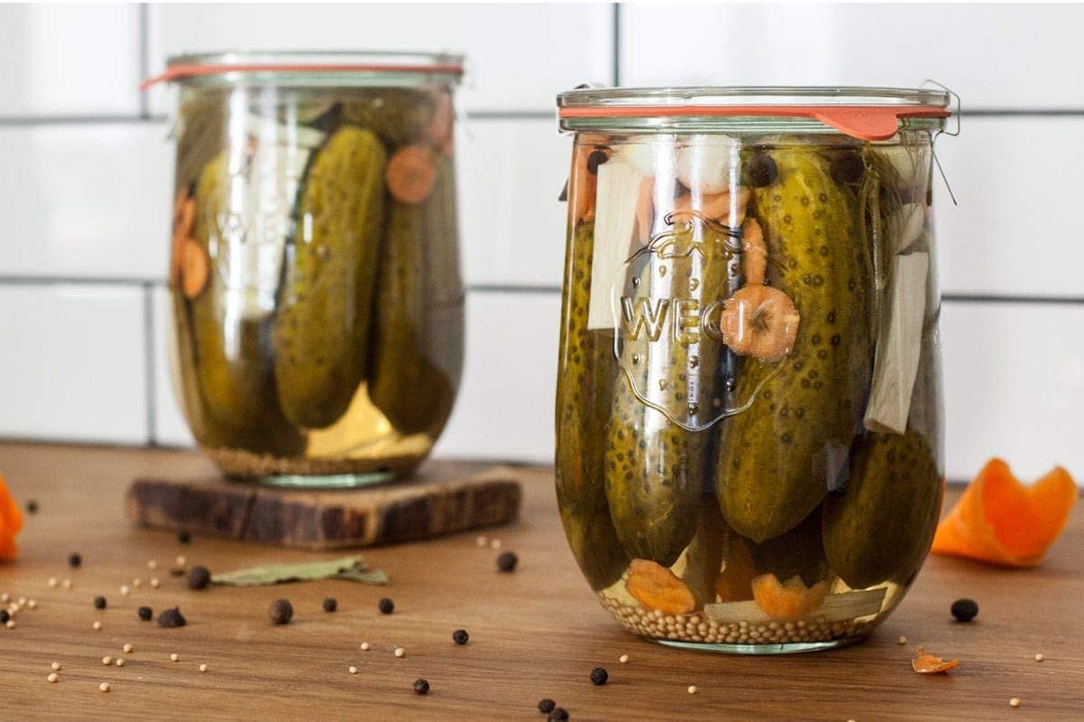 Two glass jars filled with pickles and seasonings on a wooden surface