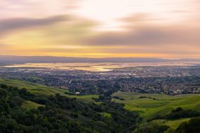 A cityscape surrounded by hills taken during sunset with a view of water bodies in the background