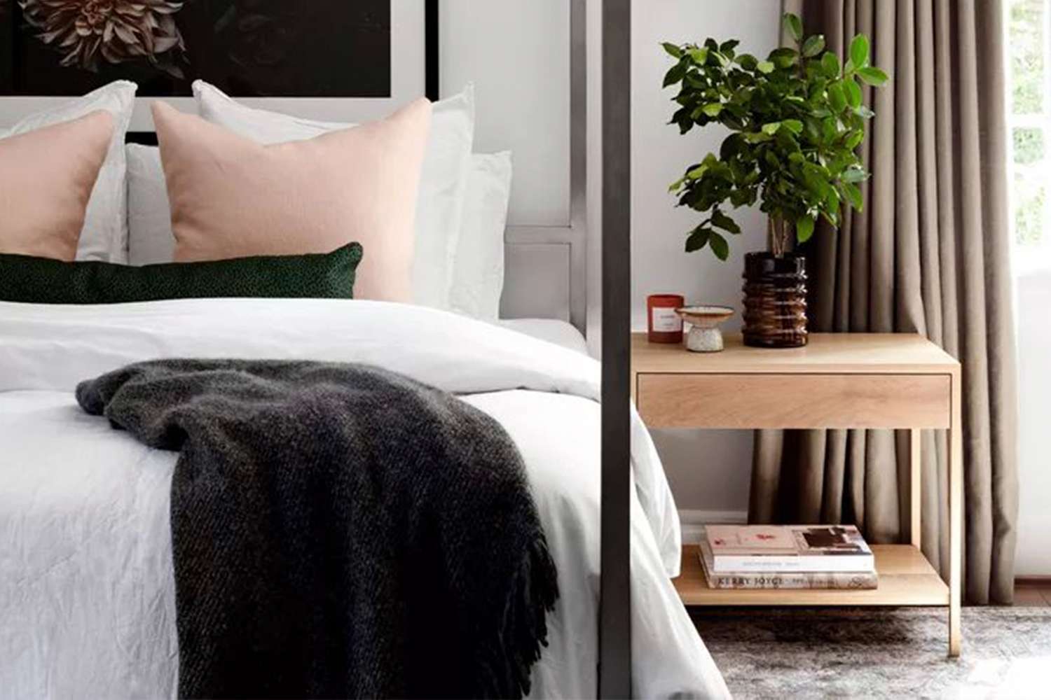 A neatly arranged bedroom with pillows a blanket on a bed and a side table holding a plant and books