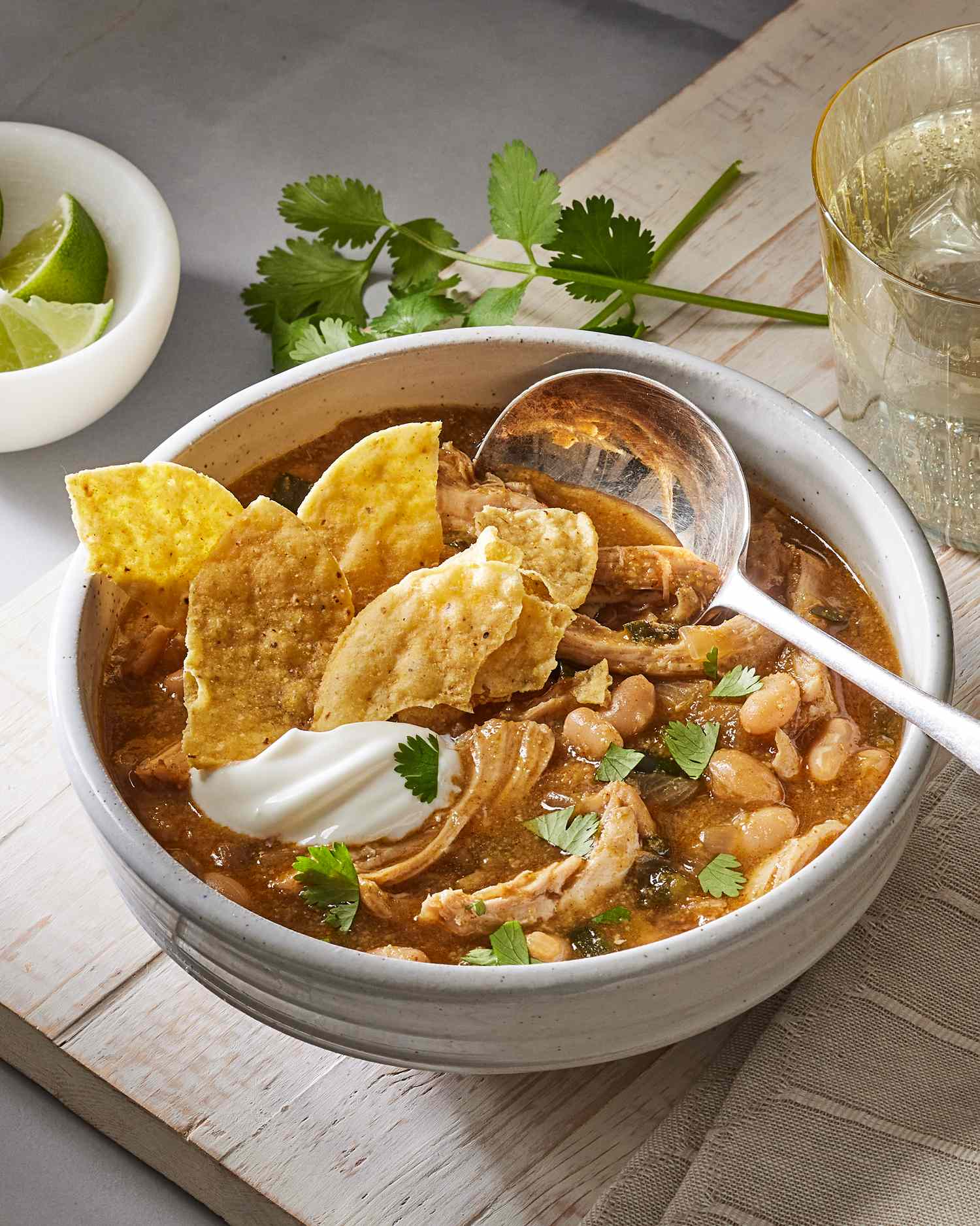 vertical format of a bowl of chicken chili with spoon and tortilla chips