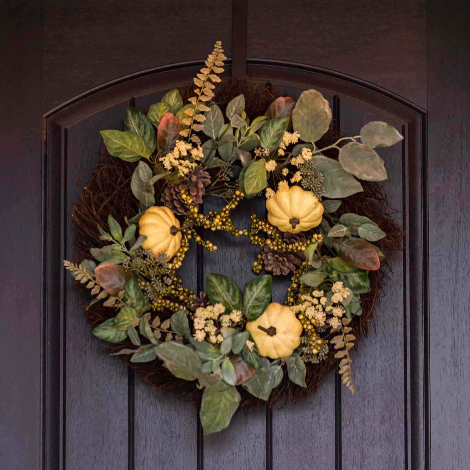 A fallthemed wreath decorated with gourds berries and leaves hanging on a dark wooden door