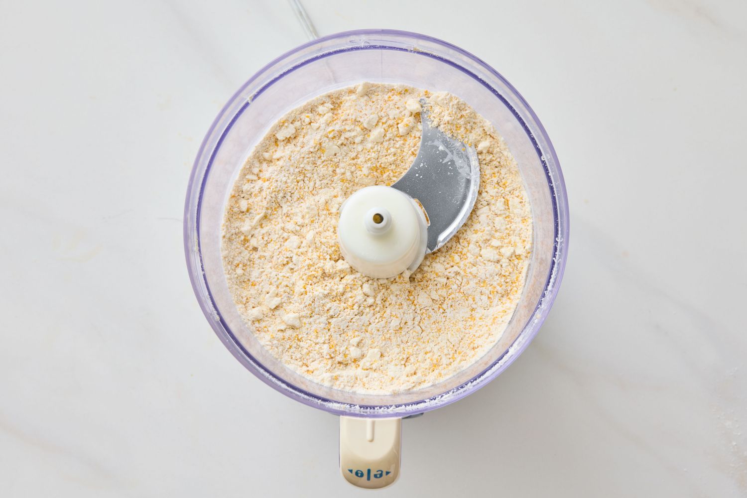 Food processor bowl filled with flour mixture and a blade attachment on a countertop
