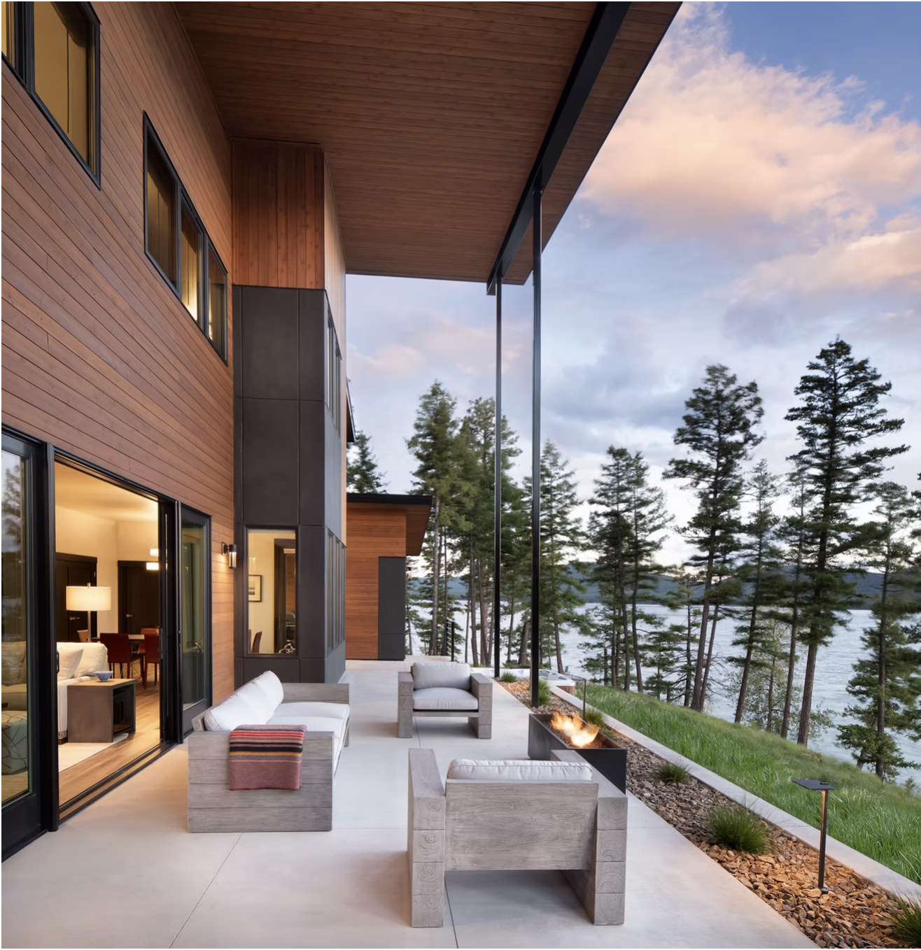 Modern patio with outdoor seating a fire pit and a view of a lake and trees