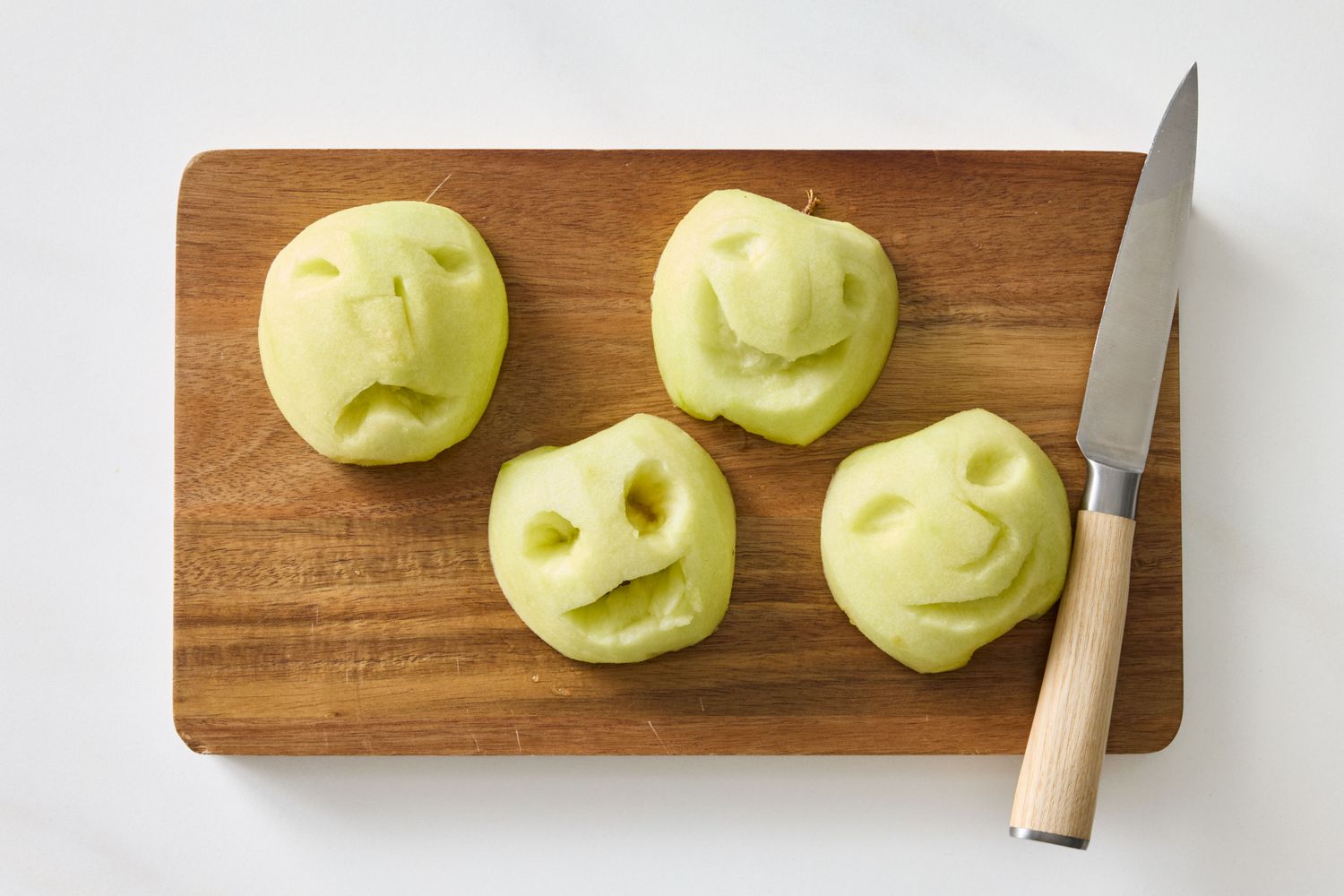 Carved apple faces placed on a wooden cutting board next to a knife