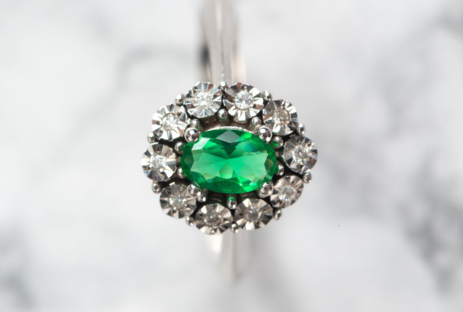 A ring with a central emerald surrounded by diamonds set in a circular arrangement