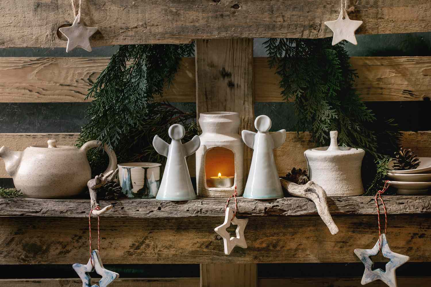 Rustic Christmasthemed decoration with ceramic figurines and a lit candle placed on a wooden shelf with star ornaments and greenery